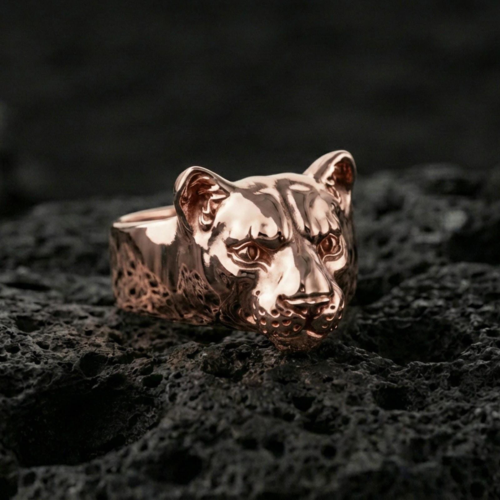 Rose gold plated puma head ring on volcanic rock, refined feline head ring with sharp eye detailing, luxury close-up