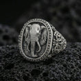 Load image into Gallery viewer, Oxidized sterling silver elephant signet ring on volcanic rock, detailed trunk and tusks with ornate engraved band, macro shot
