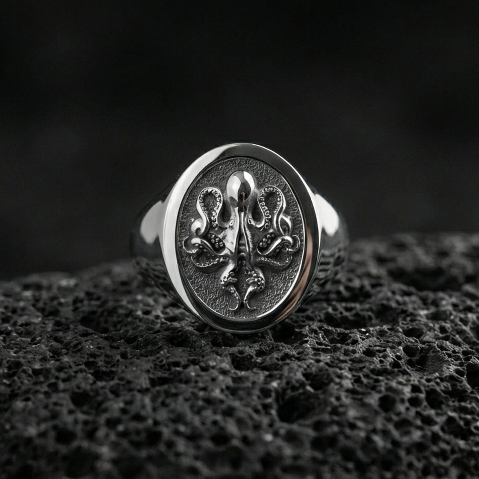 Polished silver octopus signet ring on volcanic rock, detailed sea creature octopus relief in circular bezel, clean close-up jewelry shot