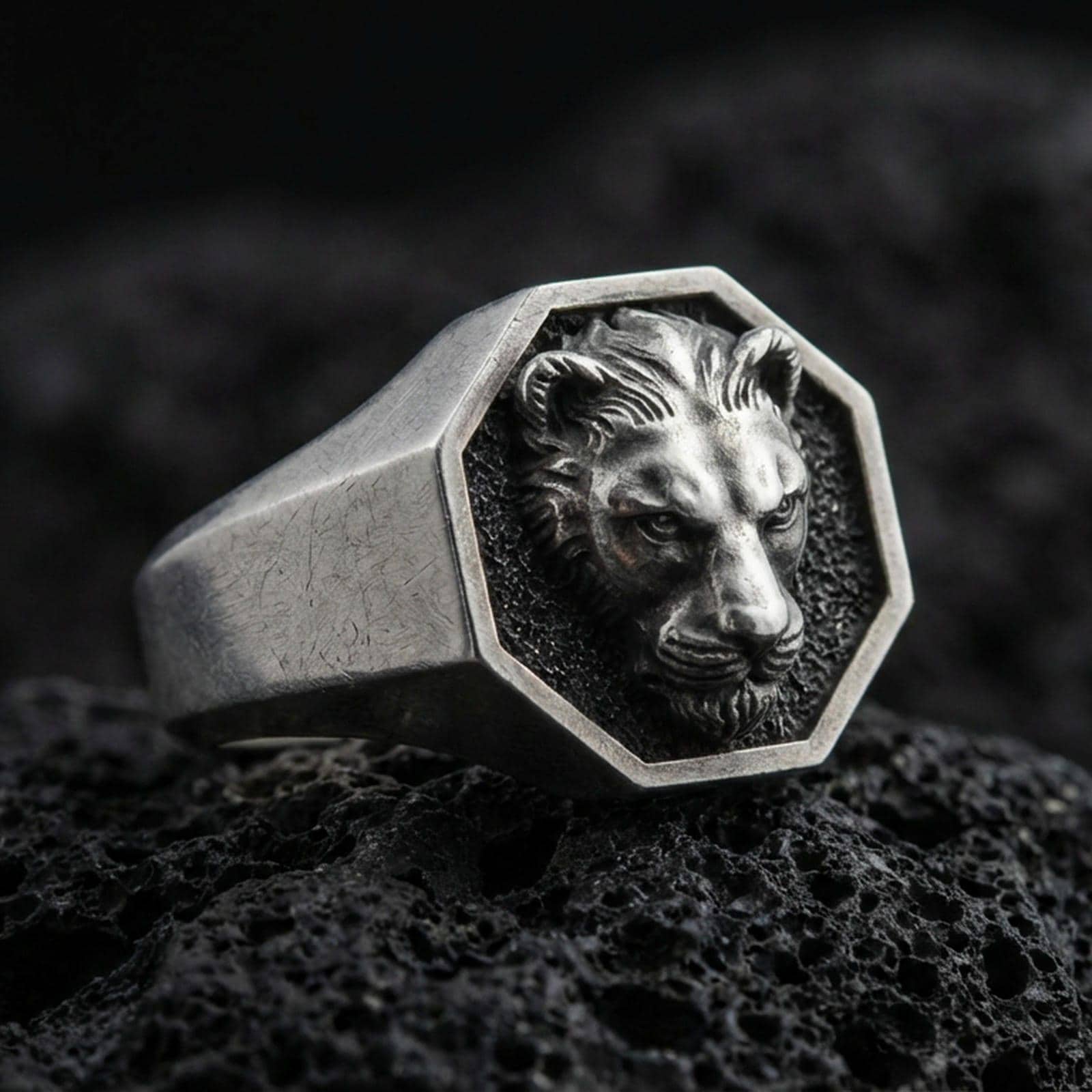 Oxidized sterling silver lioness signet ring on volcanic rock, octagon face with raised lioness head relief and dark textured background, macro product photo
