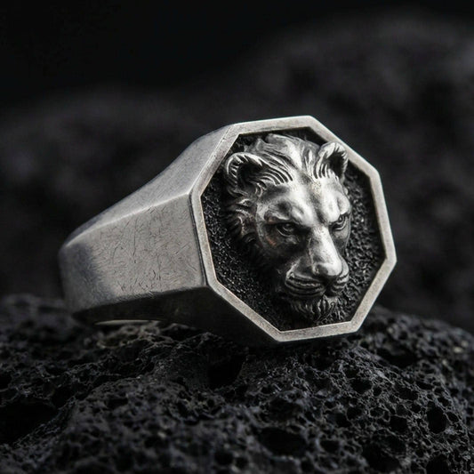 Oxidized sterling silver lioness signet ring on volcanic rock, octagon face with raised lioness head relief and dark textured background, macro product photo