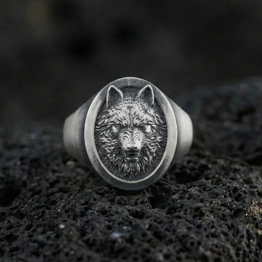 Oxidized sterling silver wolf signet ring on volcanic rock, oval face with detailed wolf head relief and dark recessed background, macro jewelry photo