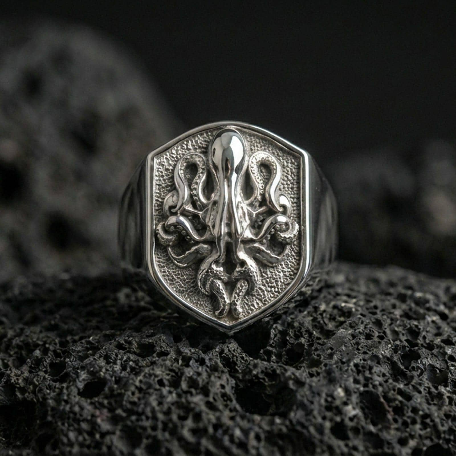 Polished silver octopus signet ring on volcanic rock, shield crest design with high-relief tentacles and crisp border edge, premium close-up shot