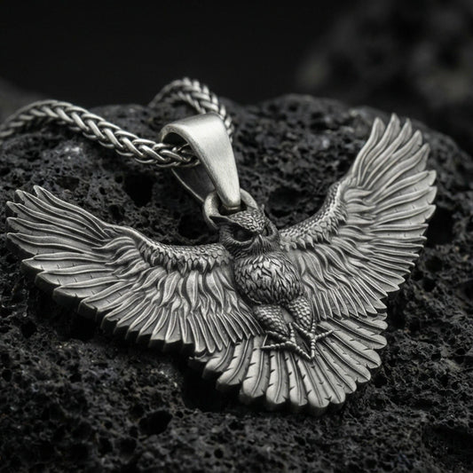 Oxidized owl pendant with spread wings on textured volcanic rock, macro close-up, dark premium studio lighting