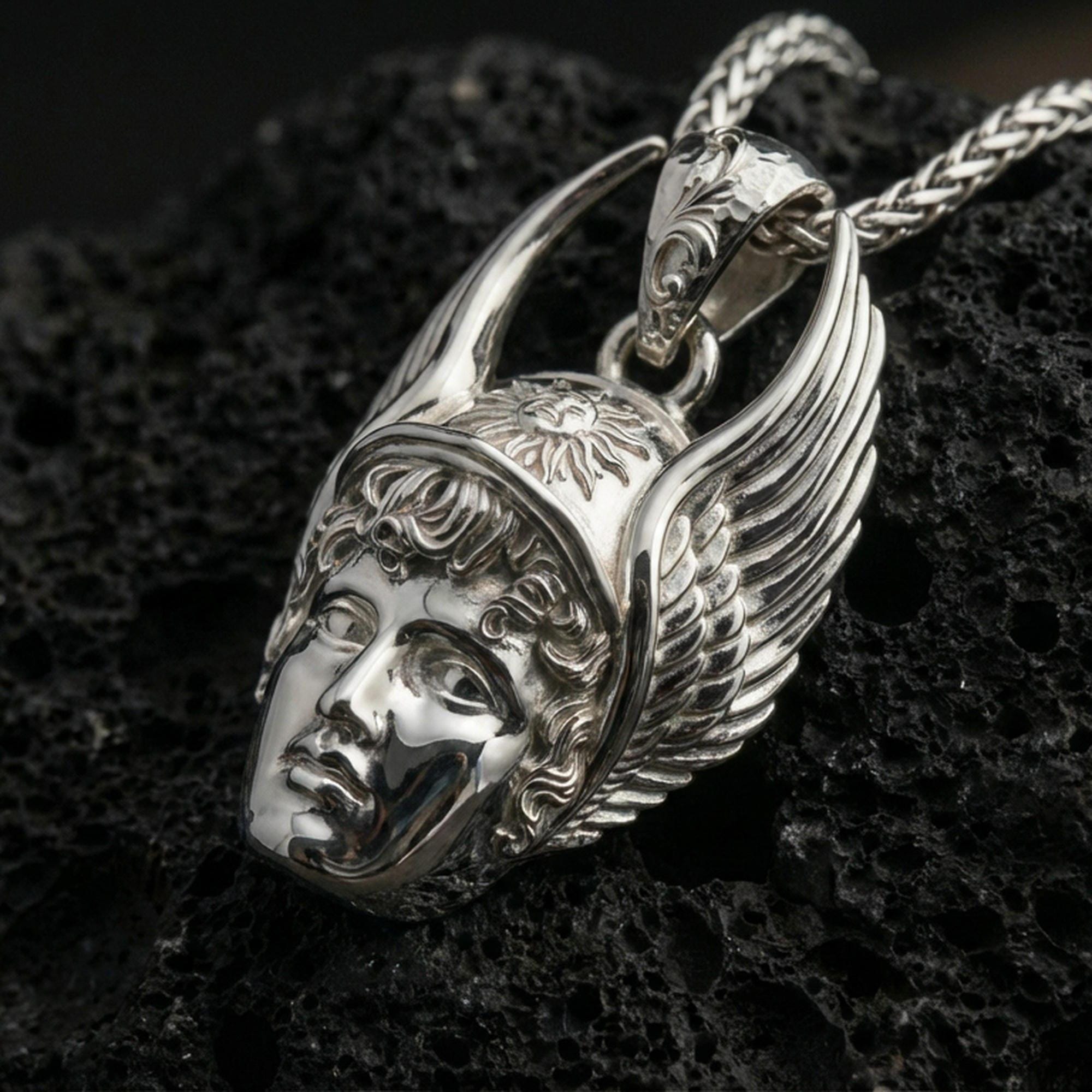 Polished silver Hermes necklace pendant on black volcanic stone background, crisp sculpted face and wings, high-end product shot