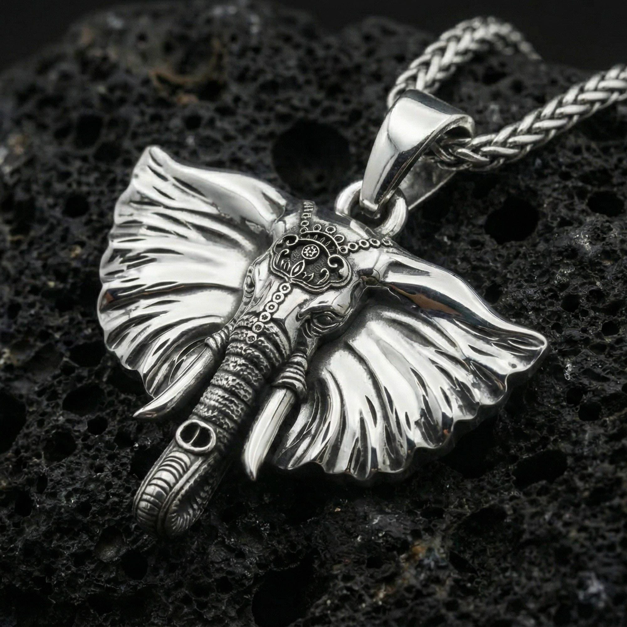 Polished silver elephant necklace pendant on black volcanic stone background, crisp sculpted textures, high-end product shot
