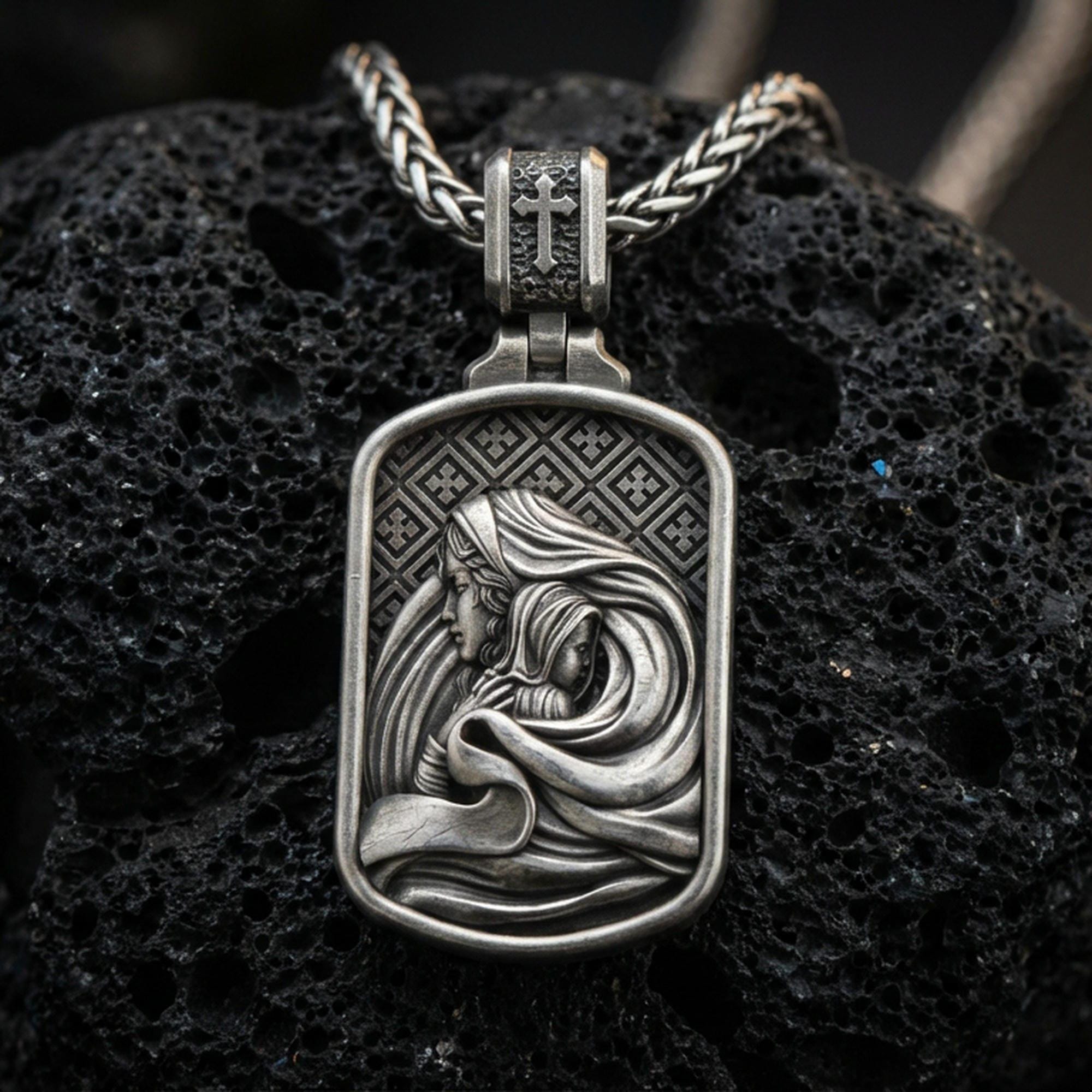 Oxidized Virgin Mary and Baby Jesus pendant on textured volcanic rock, macro close-up, Christian relief detail, premium studio lighting