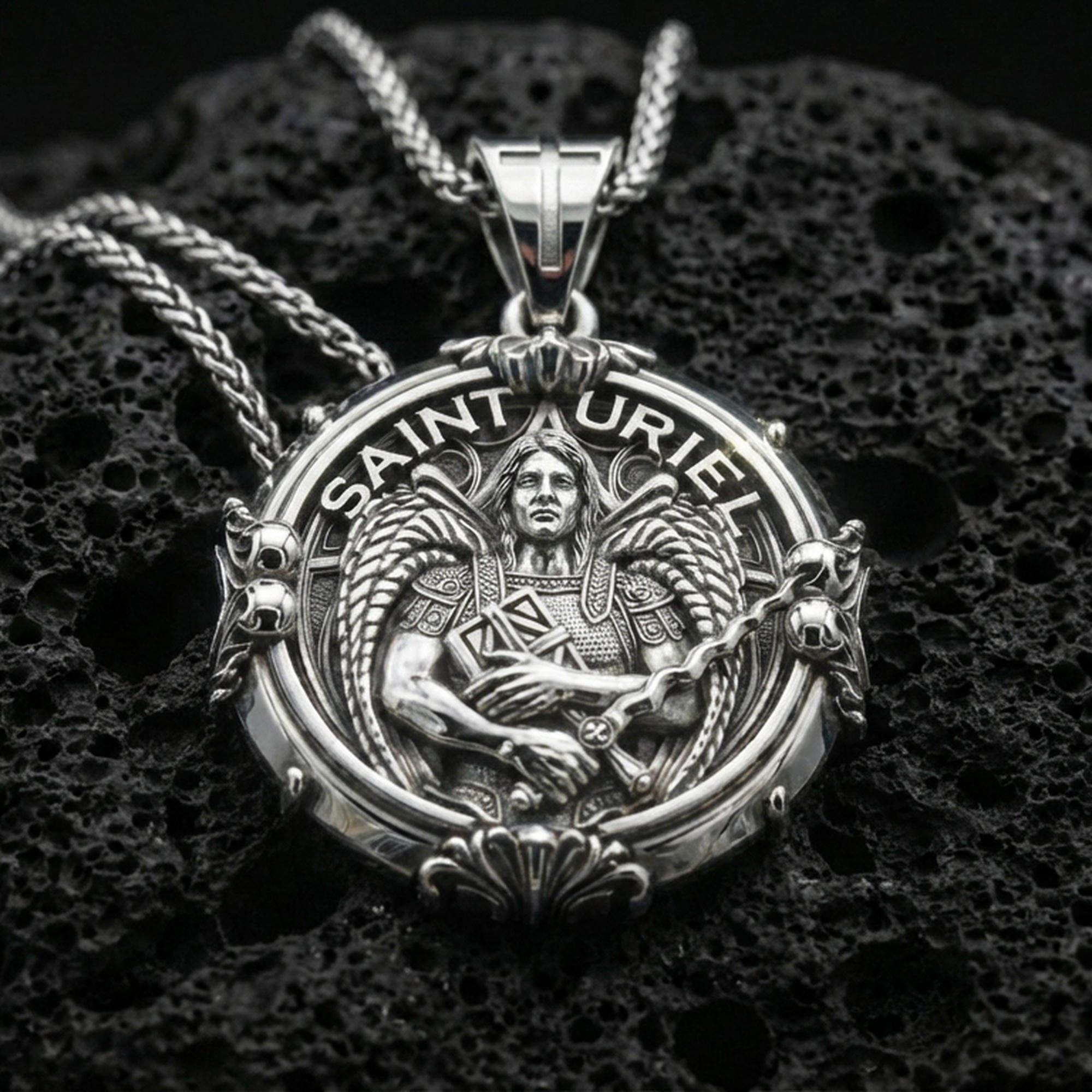 Polished silver Saint Uriel necklace pendant on black volcanic stone background, crisp angel wings and sword relief, high-end product shot