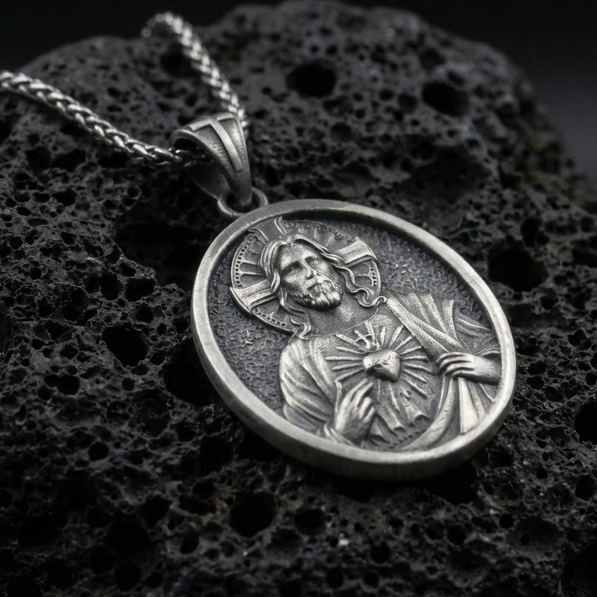 Oxidized Sacred Heart of Jesus pendant on textured volcanic rock, macro close-up, Jesus medal relief detail, premium studio lighting