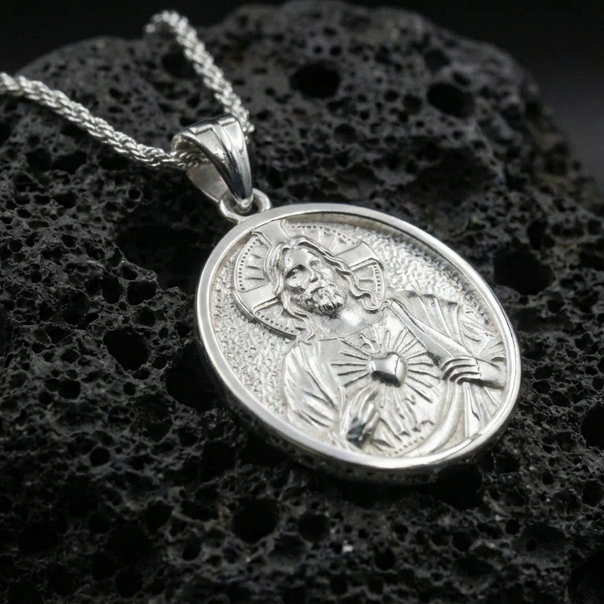 Polished silver Sacred Heart Jesus necklace pendant on black volcanic stone background, crisp halo and heart rays, high-end product shot