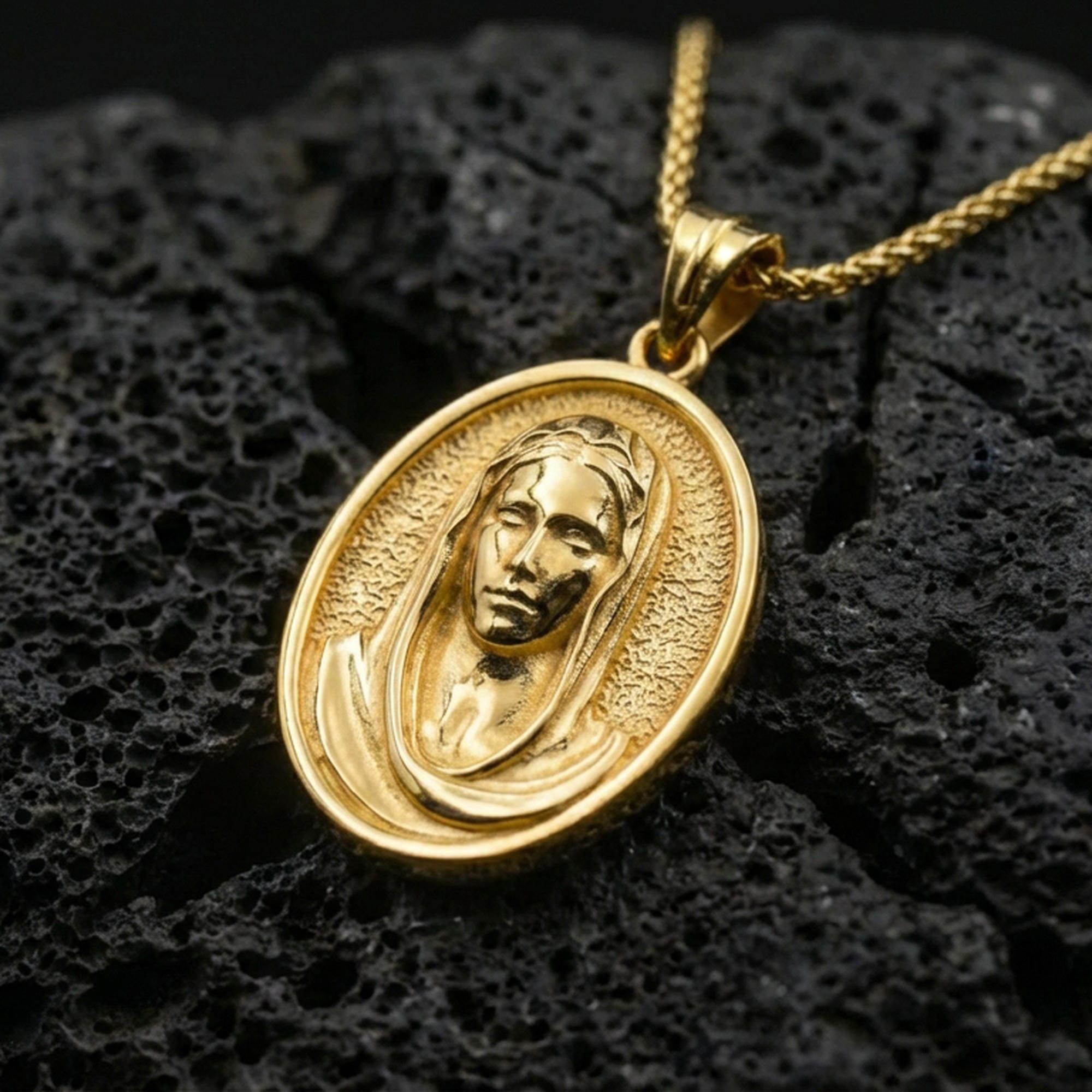 Gold plated Veiled Madonna pendant displayed on porous volcanic rock surface, close-up studio composition, detailed face relief and border