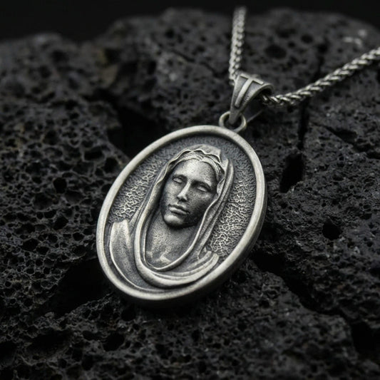 Oxidized Veiled Madonna pendant on textured volcanic rock, macro close-up, serene Virgin Mary relief detail, premium studio lighting