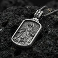 Load image into Gallery viewer, Oxidized Saint Roch dog tag pendant on textured volcanic rock, macro close-up, saint with staff and dog relief, premium studio lighting
