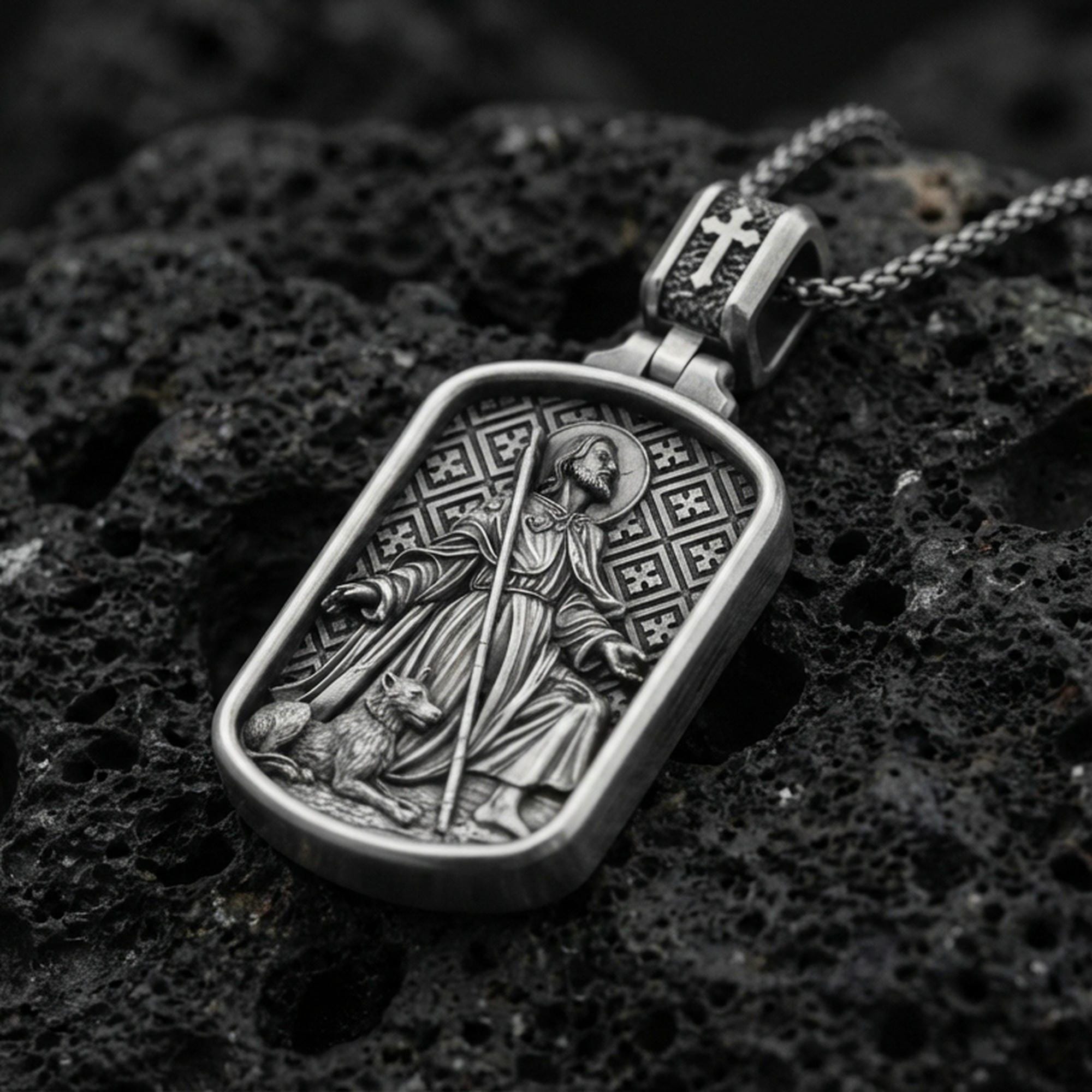 Oxidized Saint Roch dog tag pendant on textured volcanic rock, macro close-up, saint with staff and dog relief, premium studio lighting