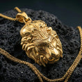 Load image into Gallery viewer, Gold plated lion head pendant necklace displayed on porous volcanic rock, royal lion design with decorative filigree, high-end studio shot
