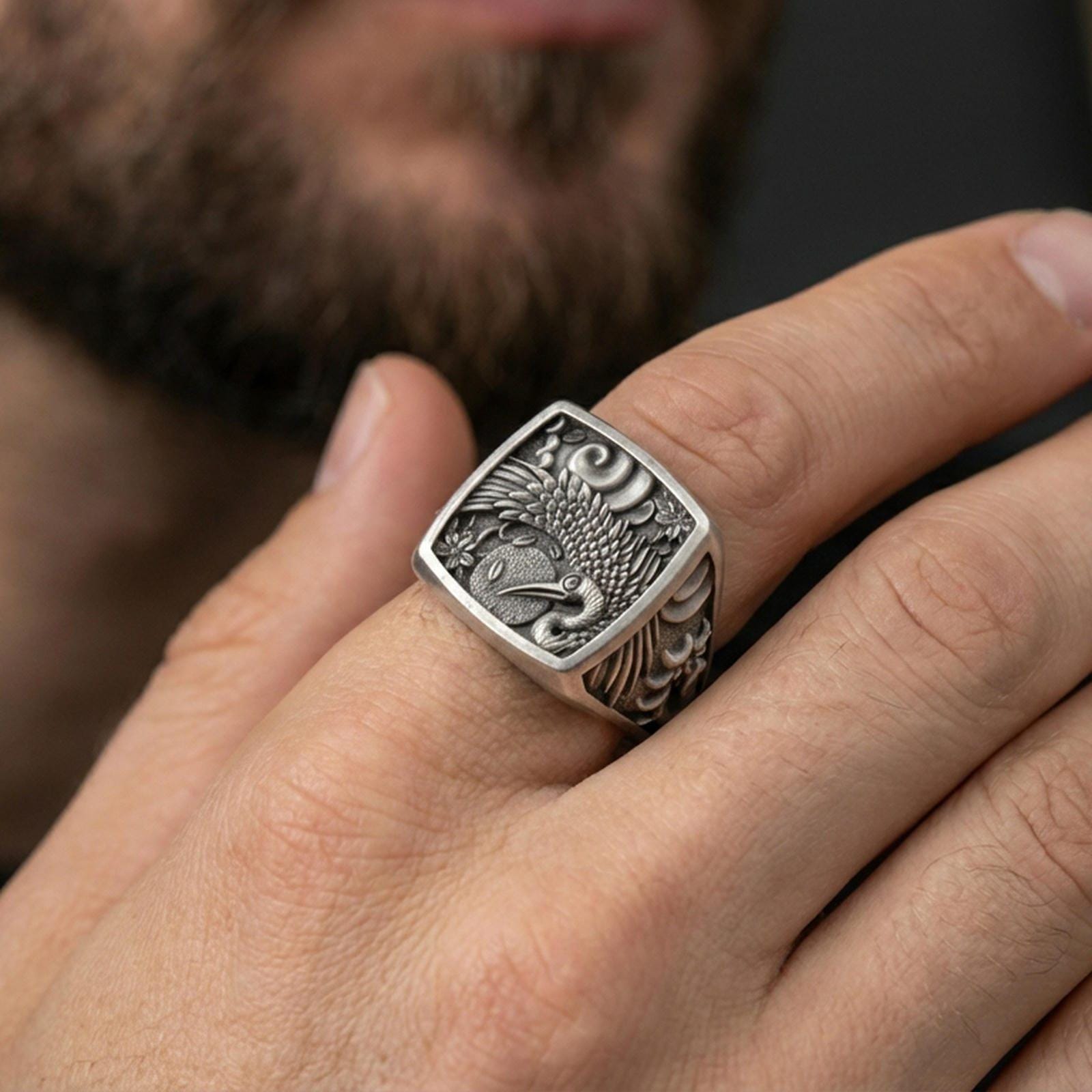 925 sterling silver crane signet ring worn on a finger, oxidized finish showing deep contrast in the crane engraving and textured panel