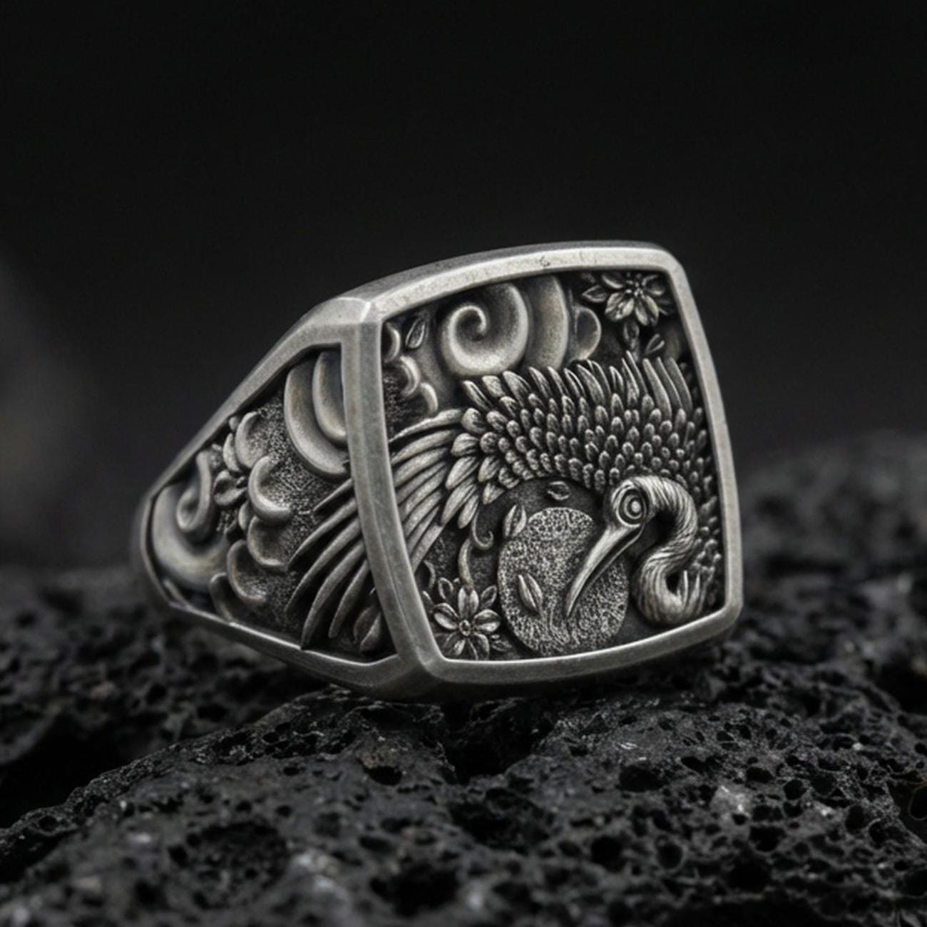 925 sterling silver crane signet ring on volcanic stone, oxidized finish highlighting the engraved feathers, floral accents, and textured background