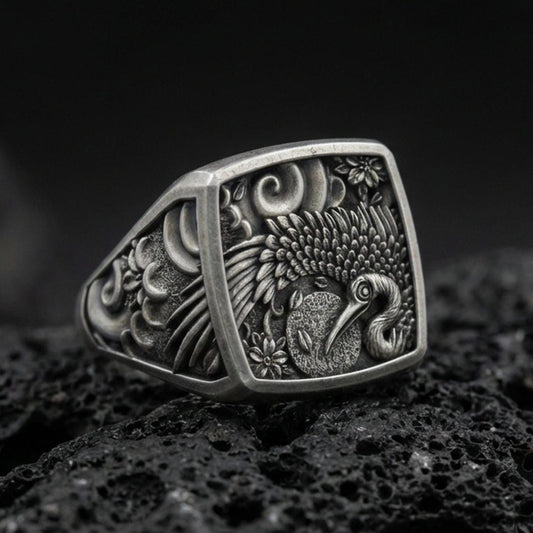 925 sterling silver crane signet ring on volcanic stone, oxidized finish highlighting the engraved feathers, floral accents, and textured background