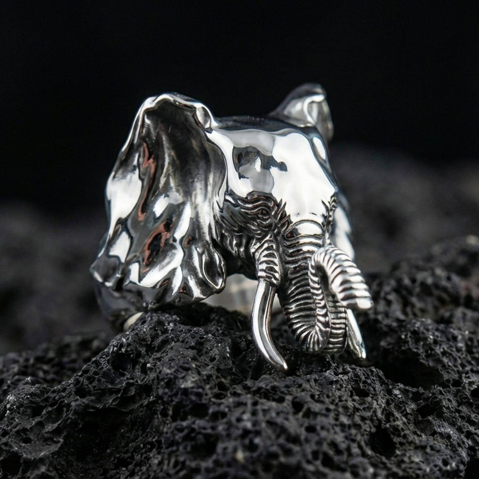 Polished silver elephant head ring on volcanic rock, macro product photo highlighting trunk and tusk details