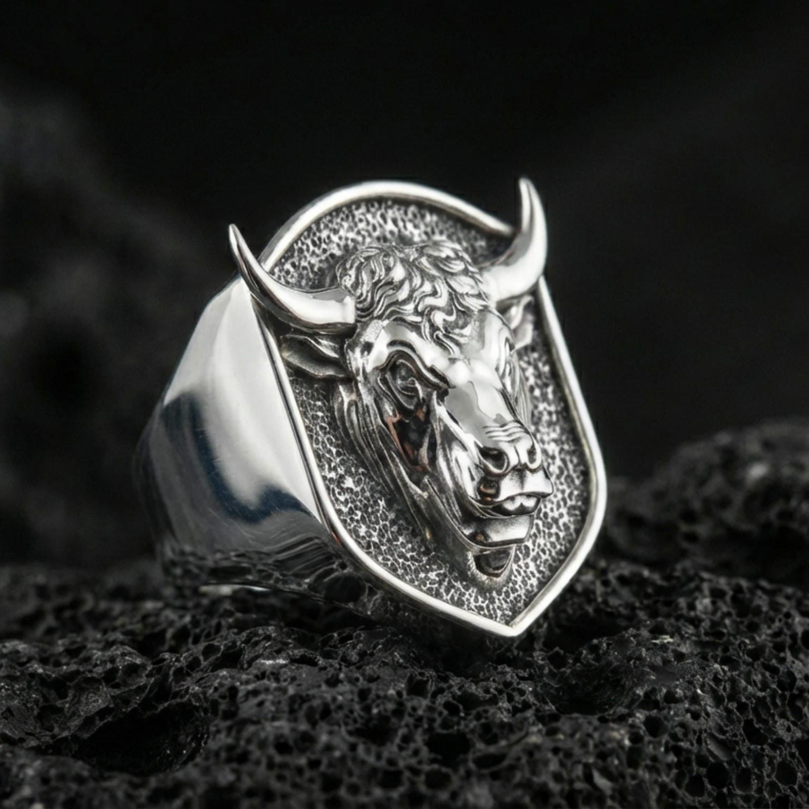 Polished silver bull head signet ring on volcanic rock surface, studio close-up highlighting crisp edges and detailed facial engraving