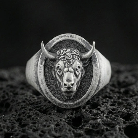 Oxidized sterling silver bull signet ring on textured volcanic rock, front-facing horned head relief with oval face in macro studio shot