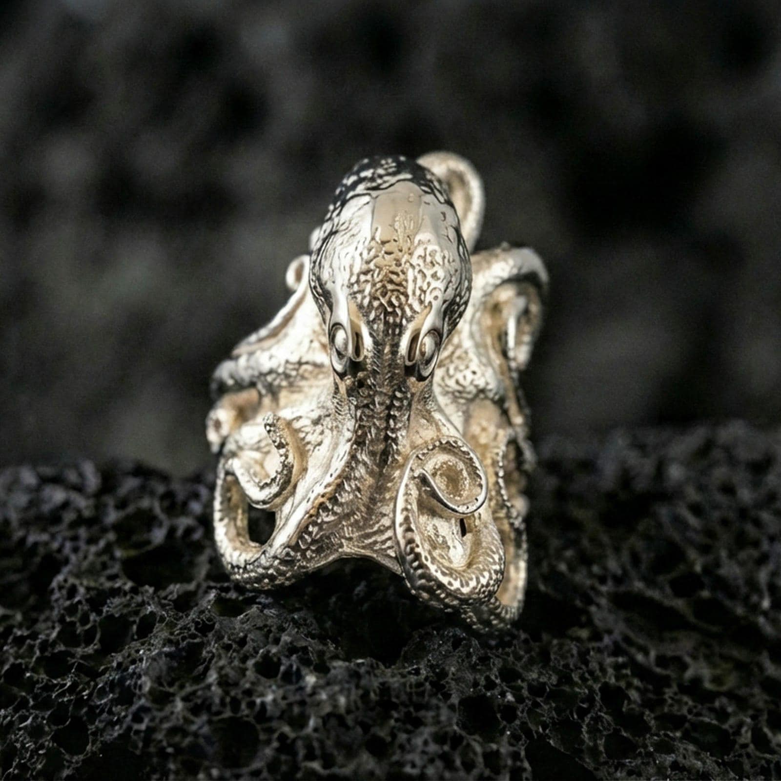 Polished silver octopus ring on volcanic rock surface, close-up highlighting the sculpted head, wrapped tentacles, and clean metal contours