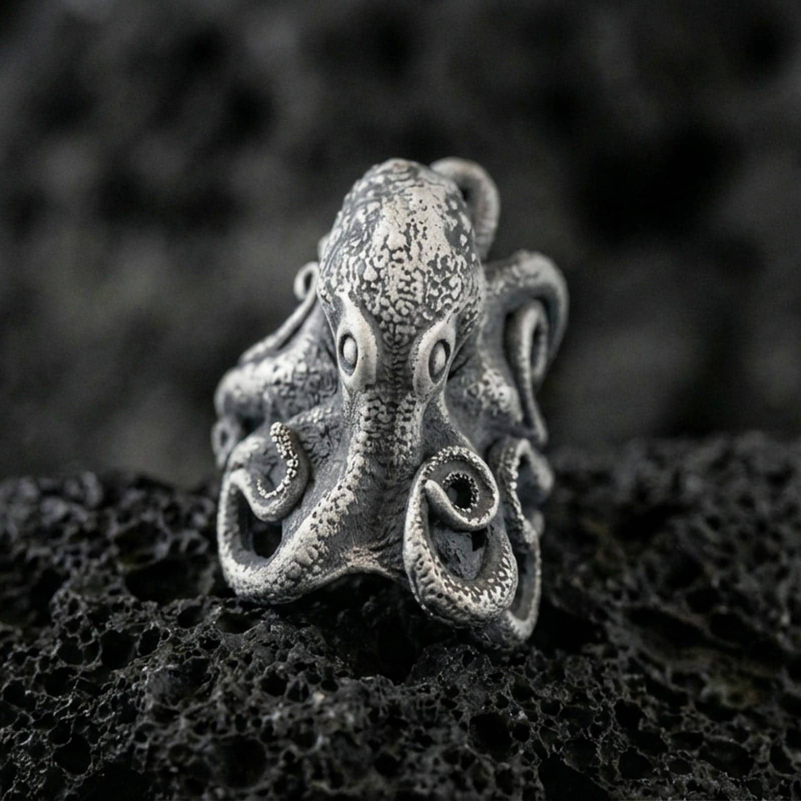 Oxidized sterling silver octopus ring on textured volcanic rock, macro close-up showing tentacle curls and speckled sea-creature texture