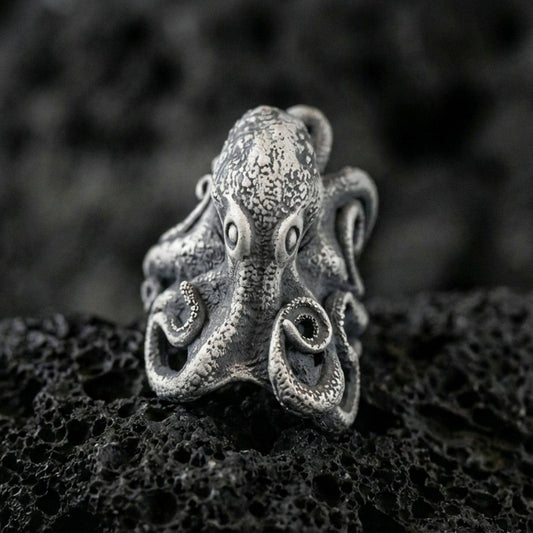 Oxidized sterling silver octopus ring on textured volcanic rock, macro close-up showing tentacle curls and speckled sea-creature texture