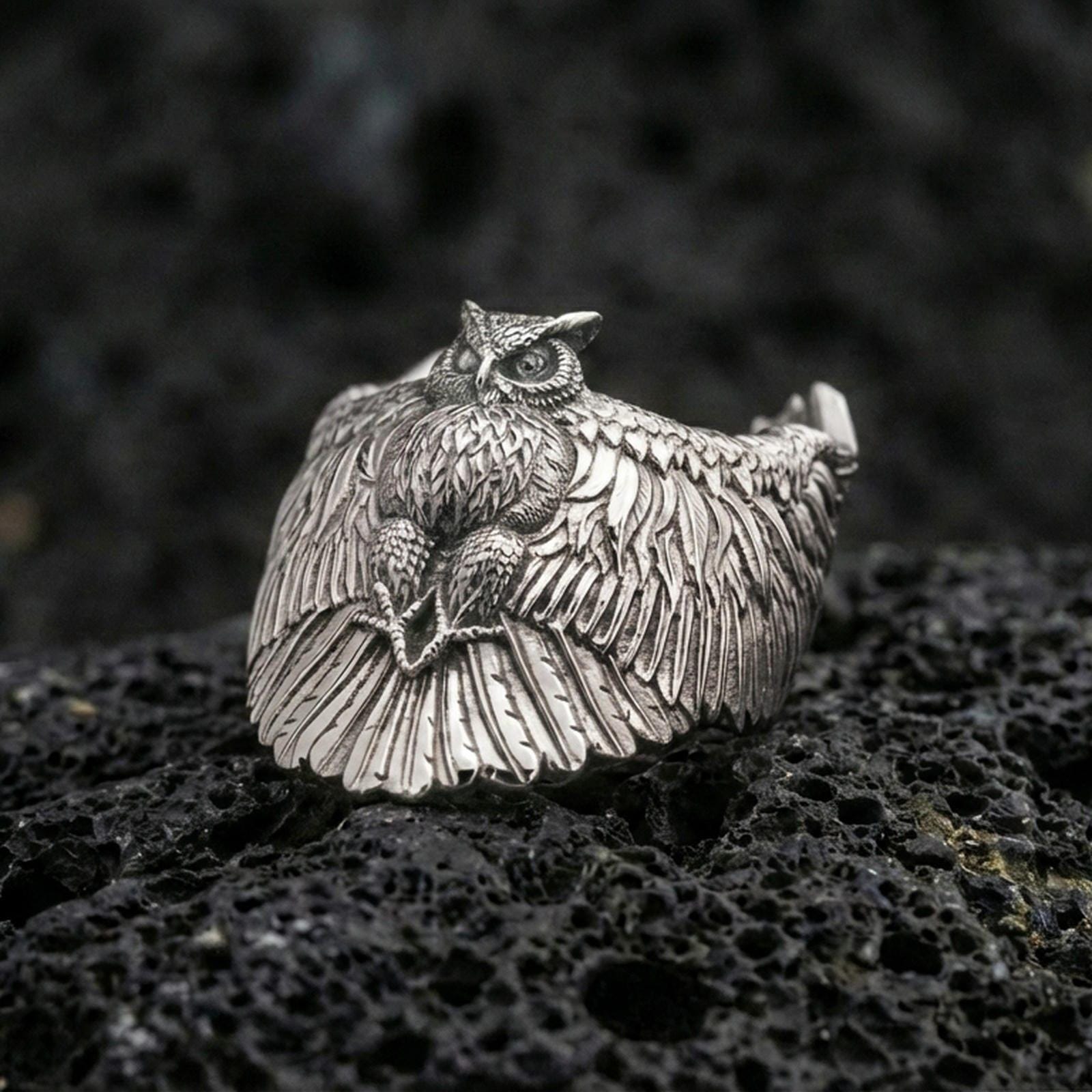 Polished silver owl ring on volcanic rock surface, close-up highlighting detailed feather texture, wide wingspan design, and clean metal contours