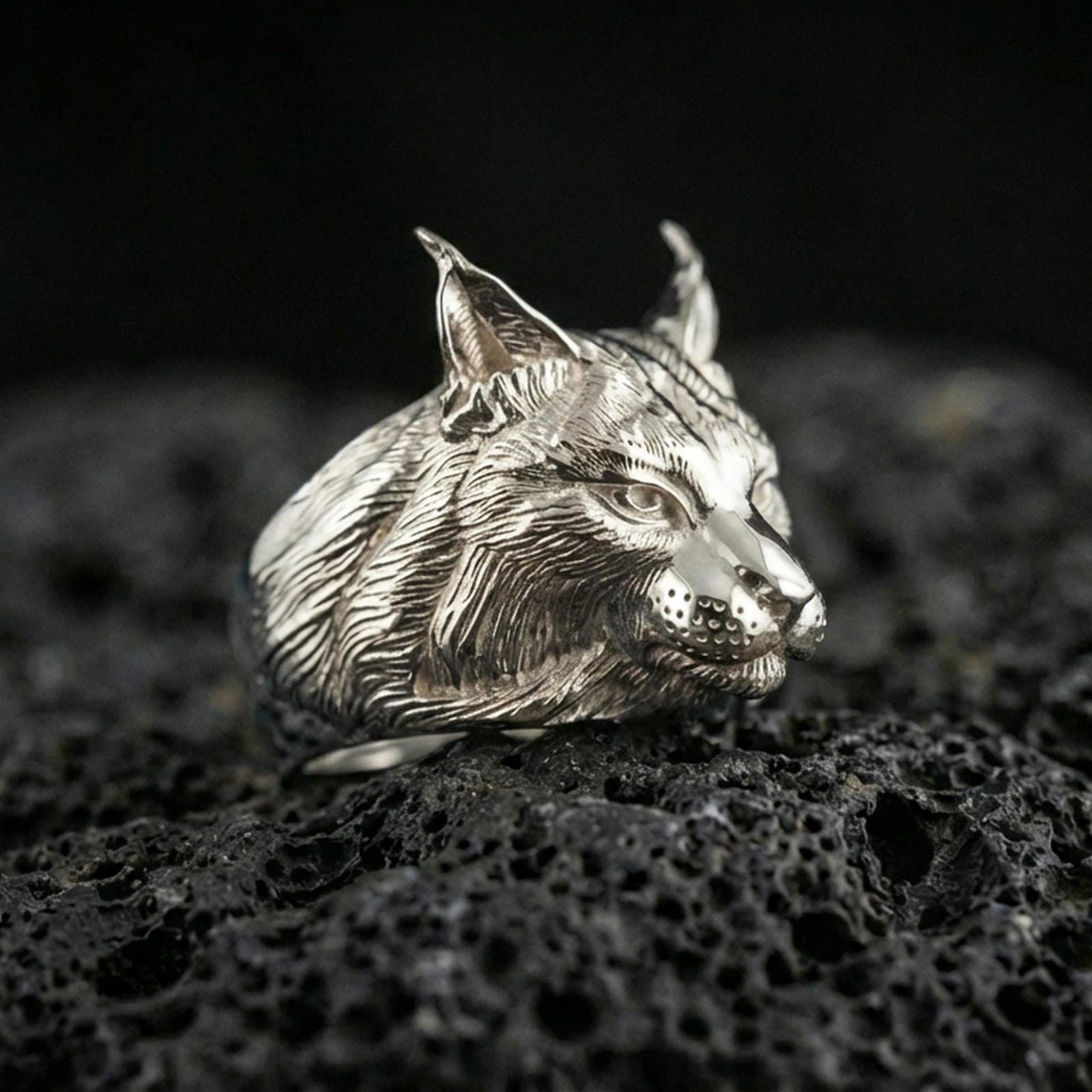 Polished silver lynx head ring on volcanic rock surface, close-up highlighting the sculpted whisker pads, sharp ear tips, and clean metal contours