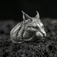 Load image into Gallery viewer, Oxidized sterling silver lynx ring on textured volcanic rock, macro close-up showing detailed fur engraving, pointed ears, and realistic feline profile
