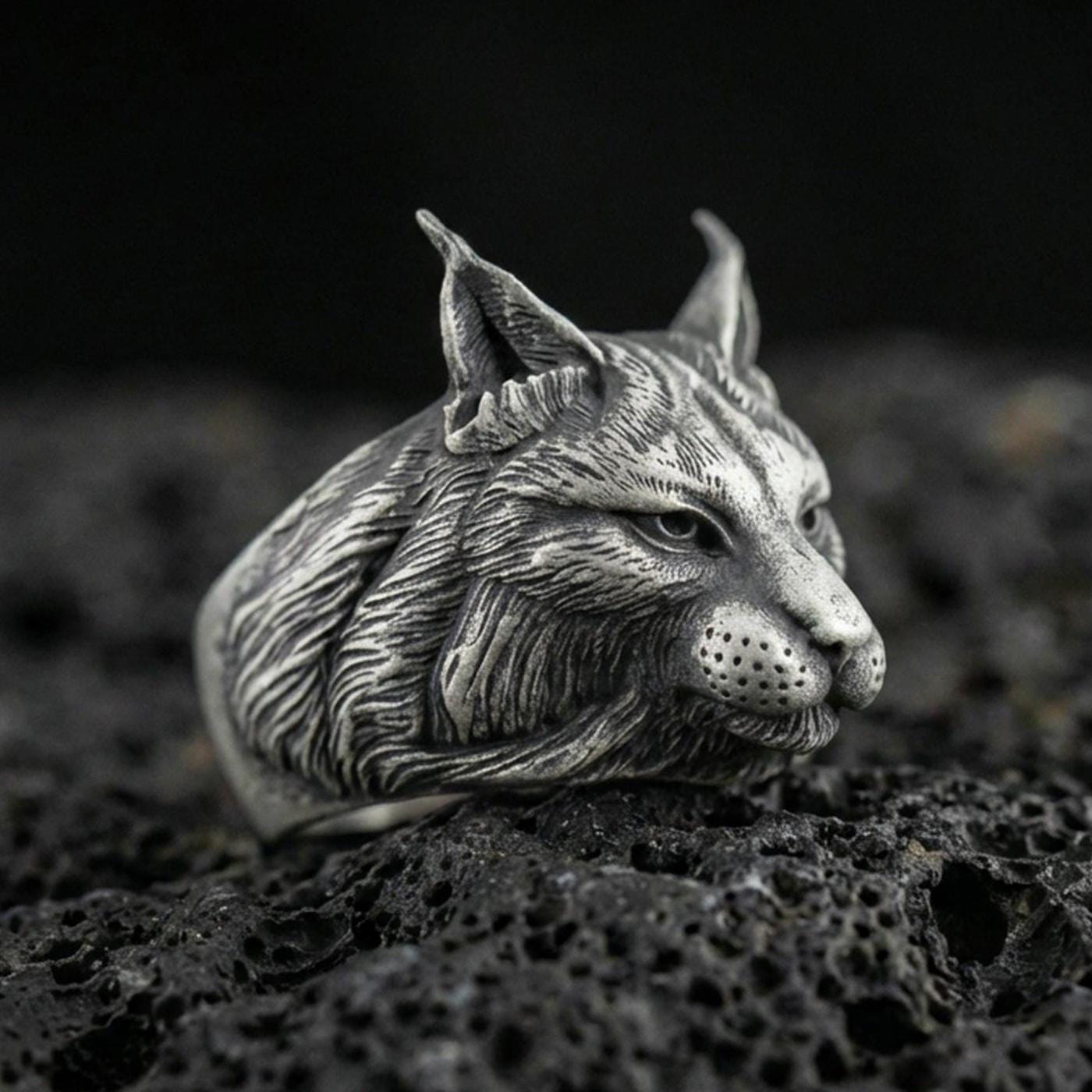 Oxidized sterling silver lynx ring on textured volcanic rock, macro close-up showing detailed fur engraving, pointed ears, and realistic feline profile
