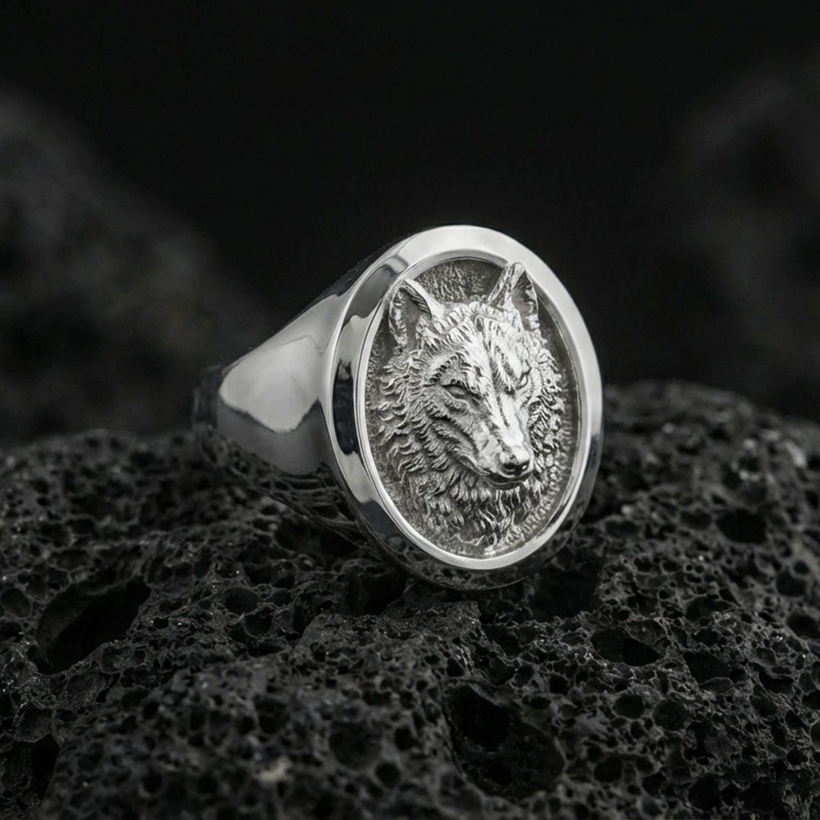 Polished silver wolf head ring on volcanic stone, crisp fur detailing and oval bezel profile