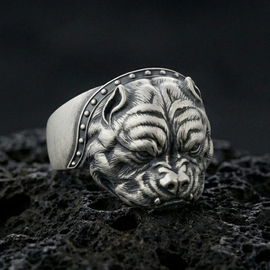 Oxidized sterling silver bulldog head ring on textured volcanic rock, macro close-up showing intense facial wrinkles and studded collar detail