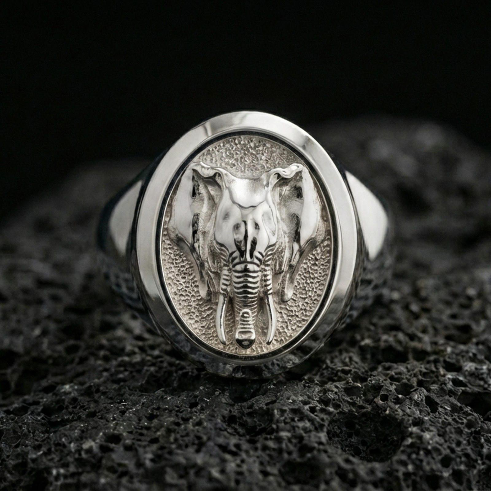 Polished silver elephant head signet ring on volcanic rock surface, close-up highlighting the oval bezel, textured background, and clean band profile