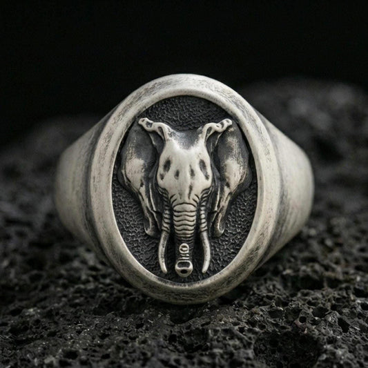 Oxidized sterling silver elephant signet ring on textured volcanic rock, macro close-up showing oval face with frontal elephant head, tusks, and trunk detail