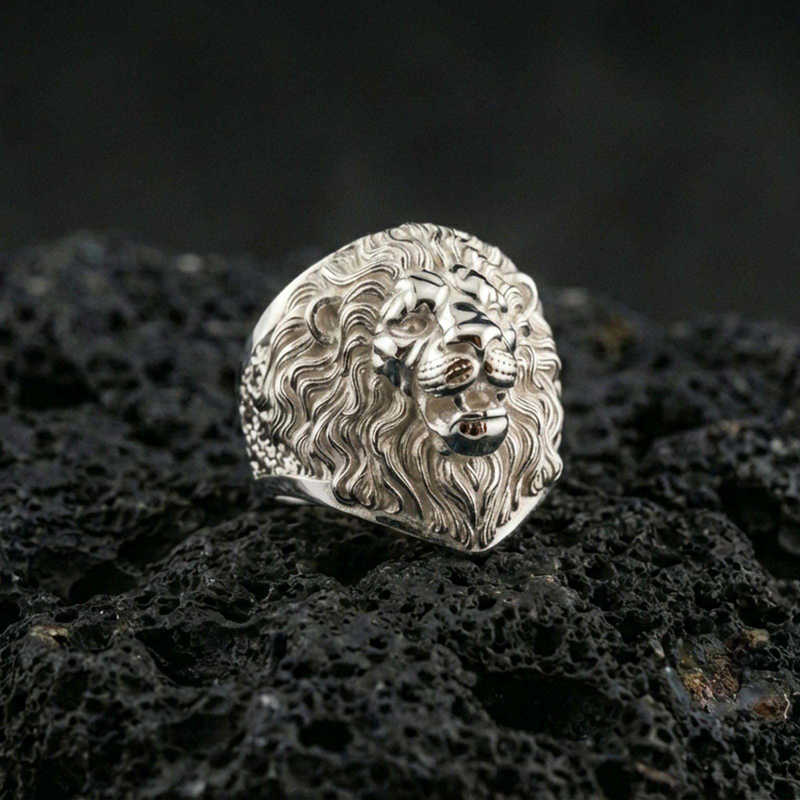 Polished silver lion ring on volcanic rock surface, close-up highlighting the layered mane texture, defined whisker pads, and clean ring profile
