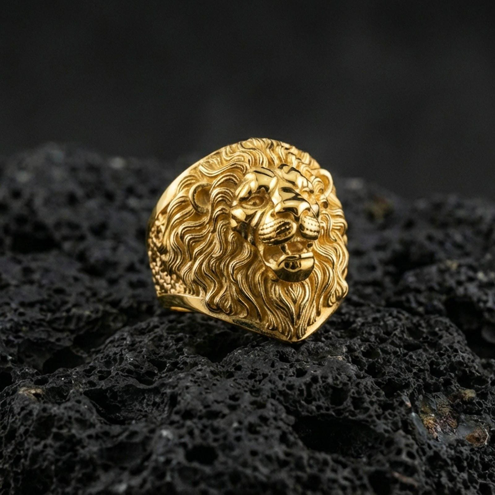 Gold plated lion head ring on porous volcanic stone, premium dark studio shot emphasizing the bold mane relief and fierce animal expression