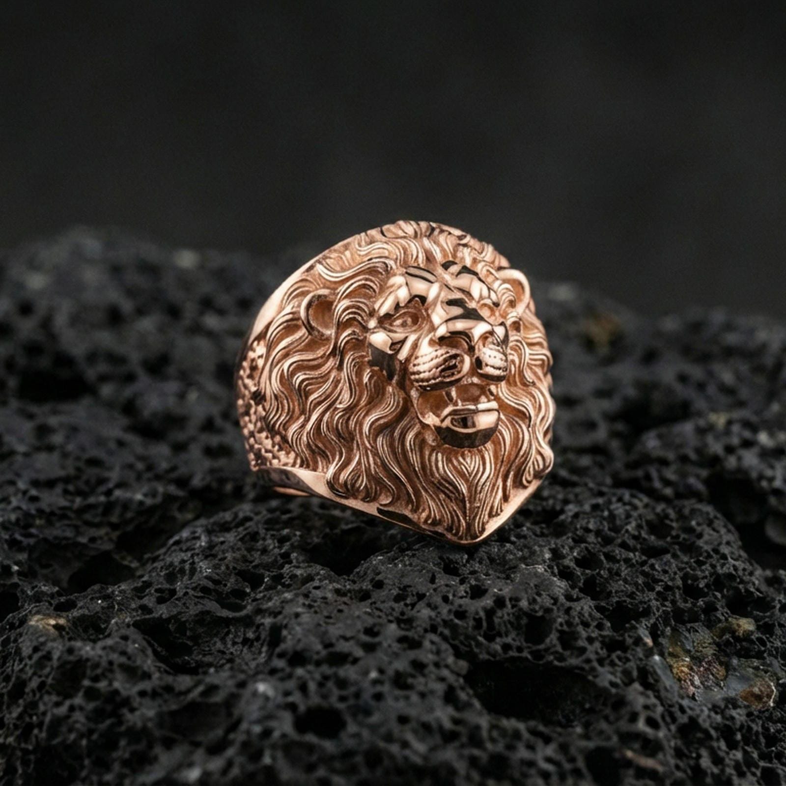 Rose gold plated lion ring on volcanic rock, sharp macro product photo showcasing the roaring lion face and intricate mane engraving