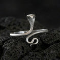 Load image into Gallery viewer, Polished silver cobra ring on volcanic rock surface, close-up highlighting the sleek coiled shape, hooded head, and crisp scale engraving
