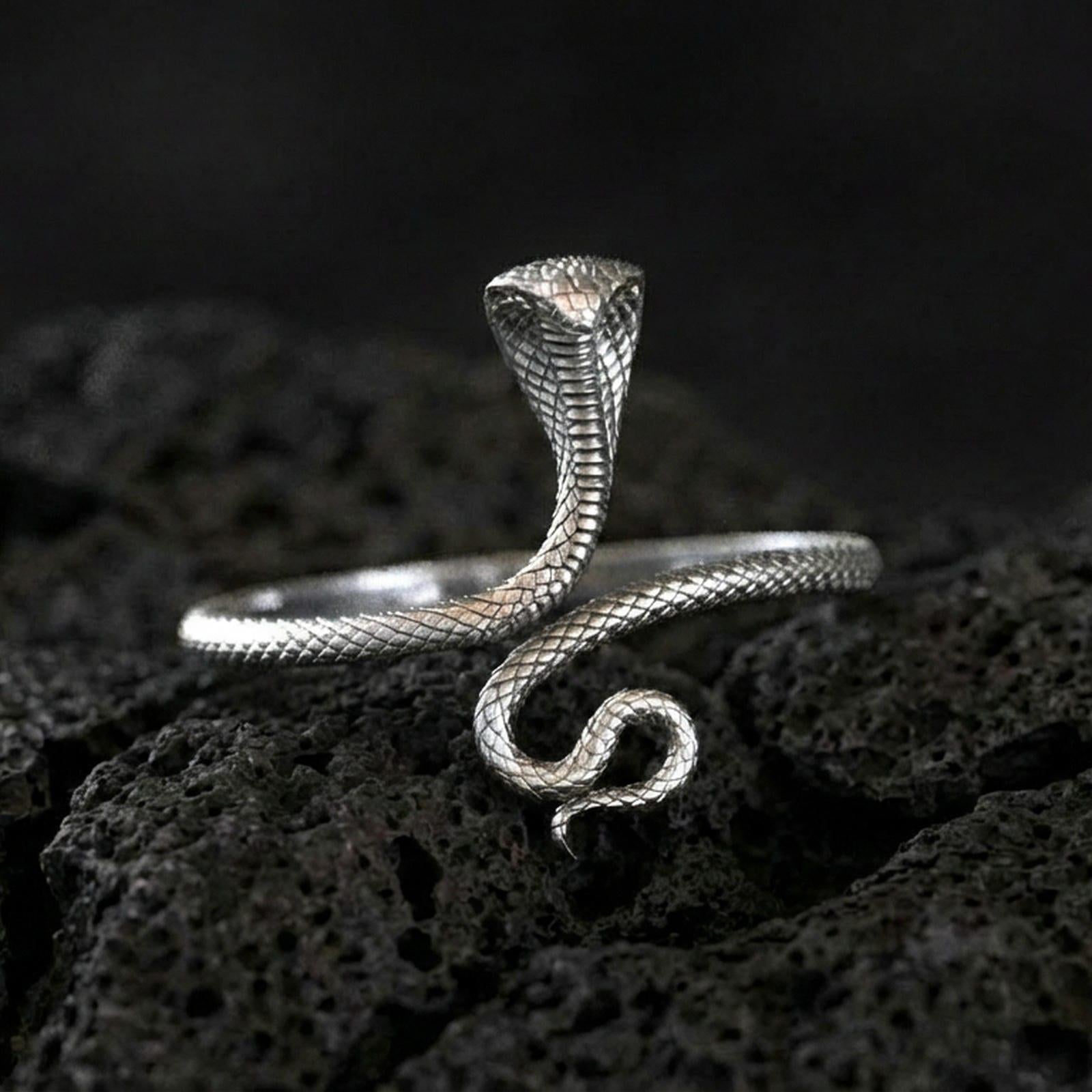 Polished silver cobra ring on volcanic rock surface, close-up highlighting the sleek coiled shape, hooded head, and crisp scale engraving