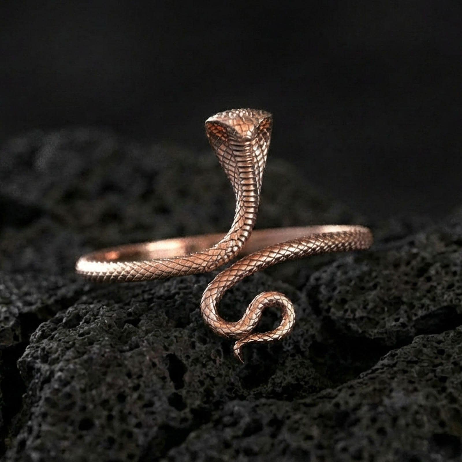 Rose gold plated cobra ring on volcanic rock, sharp macro product photo showcasing the hooded snake pose and intricate scale detailing