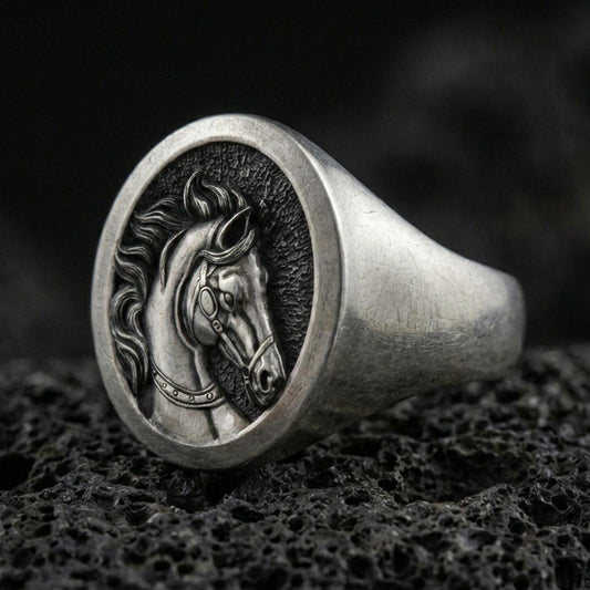 Oxidized sterling silver horse signet ring on textured volcanic rock, macro close-up showing round face with engraved stallion portrait and dark recessed background