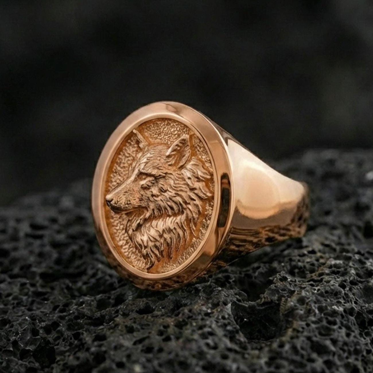 Rose gold plated wolf signet ring on volcanic rock, detailed wolf profile with luxury warm metal tone