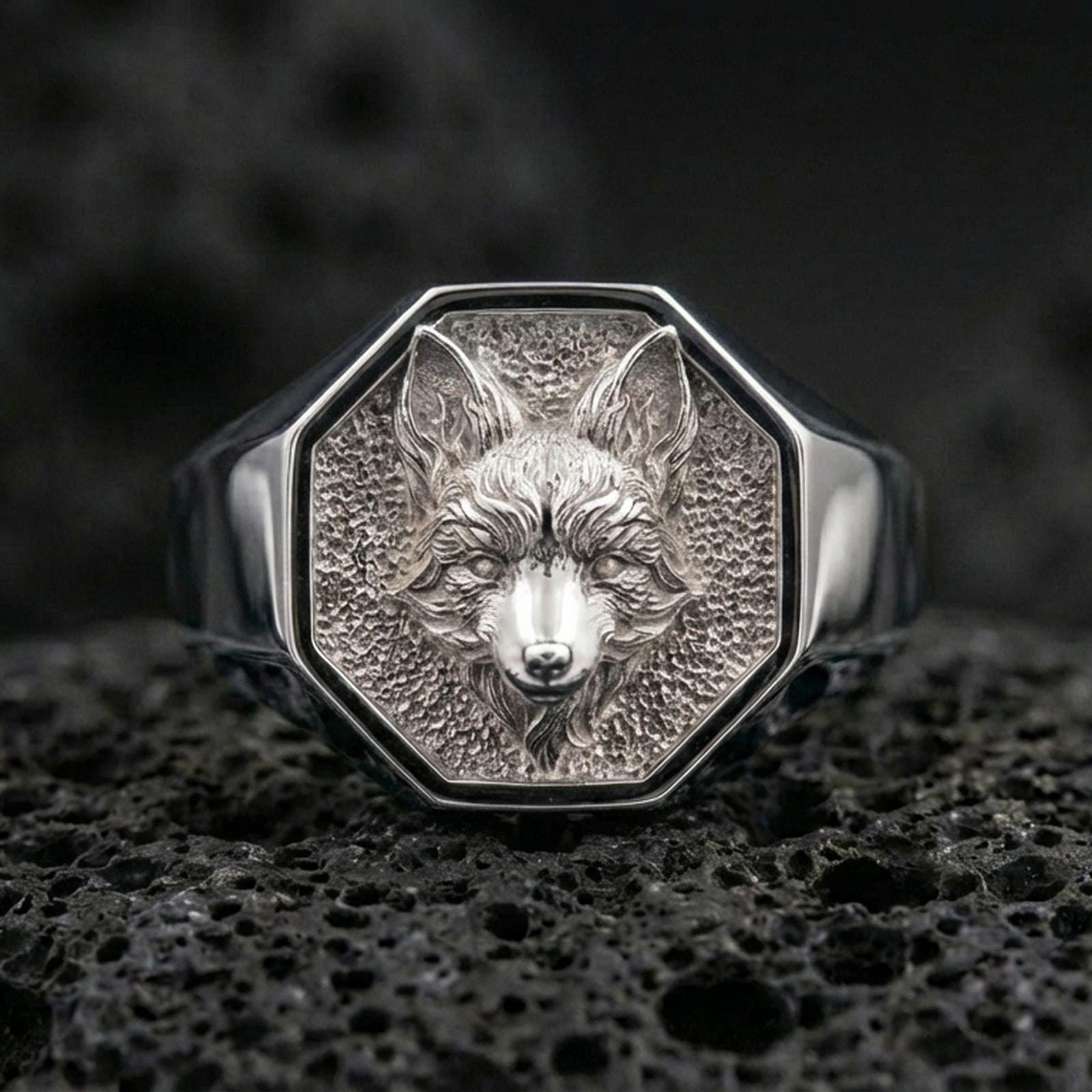 Front view of a polished silver fox head signet ring on textured volcanic rock with premium macro lighting