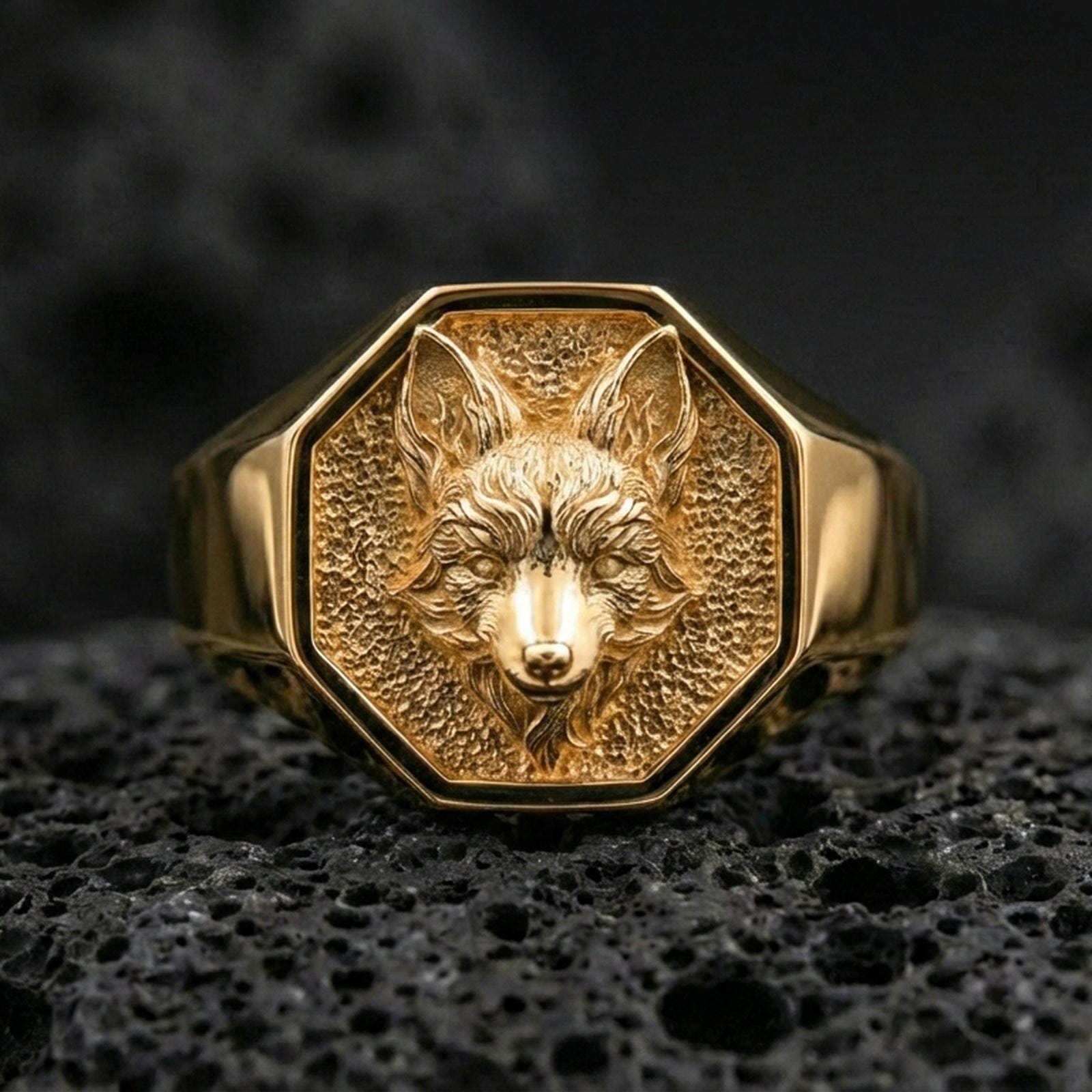 Detailed gold plated fox signet ring photographed on black volcanic stone with sharp focus and dramatic shadows
