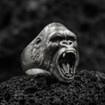 Load image into Gallery viewer, Close-up of an oxidized sterling silver gorilla head ring on porous volcanic rock in a dark studio macro shot
