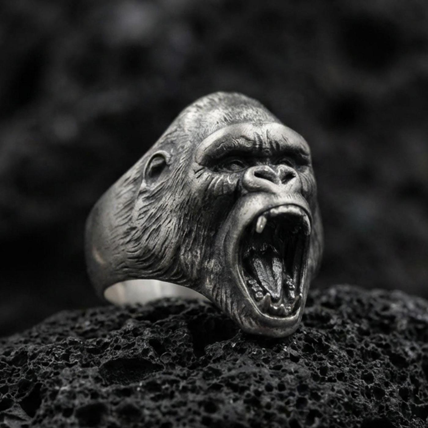 Close-up of an oxidized sterling silver gorilla head ring on porous volcanic rock in a dark studio macro shot