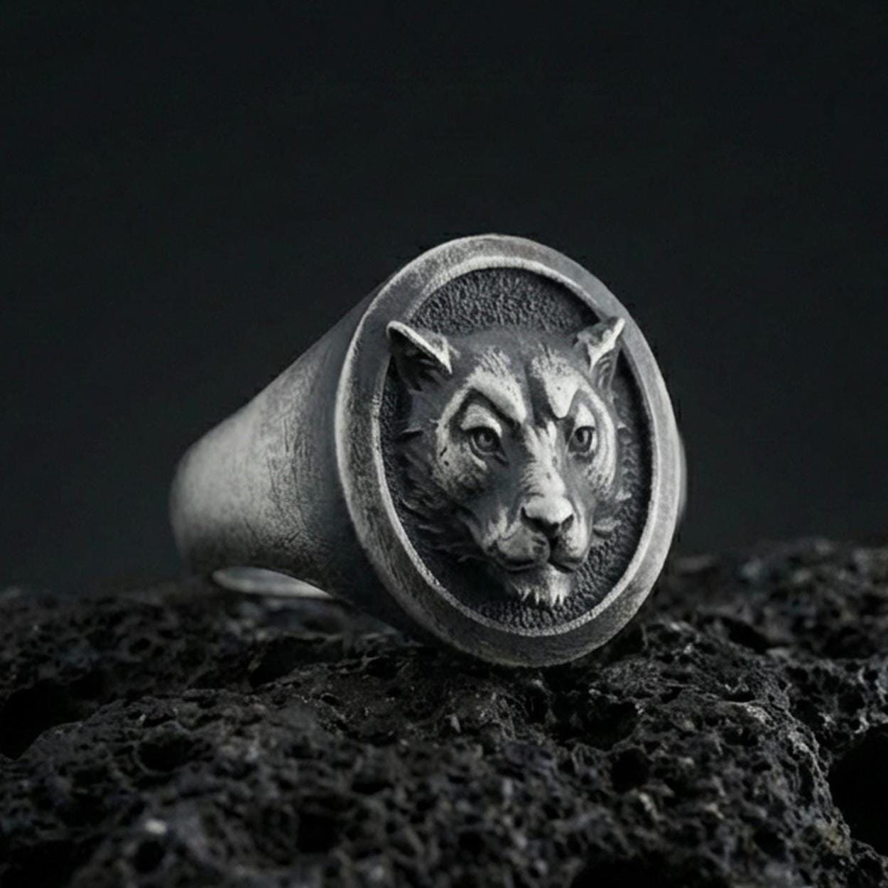 Oxidized sterling silver leopard signet ring on textured volcanic rock, macro close-up showing round face with raised big cat portrait and dark recessed background