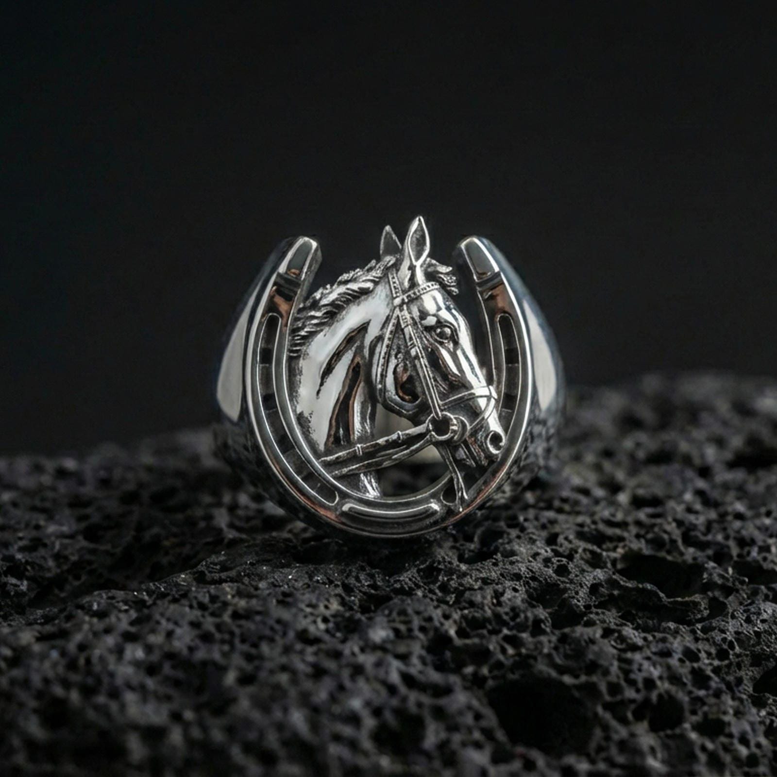 Polished silver horseshoe horse ring on volcanic rock surface, close-up highlighting the open horseshoe frame, detailed mane texture, and bridle engraving